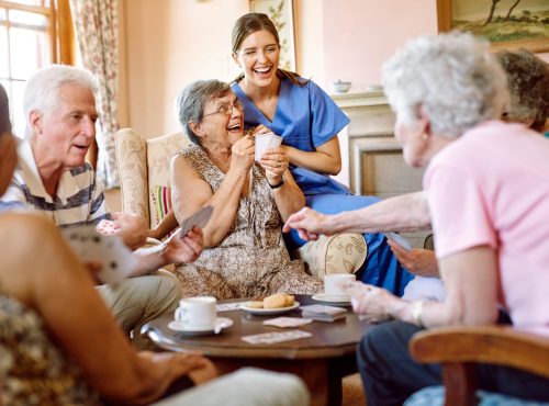 Shot of a group of happy seniors playing a card game in their retirement home while a nurse watches.